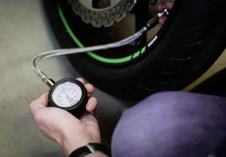 Mano revisando la presión neumaticos moto con un manómetro. El neumático tiene detalles verdes.