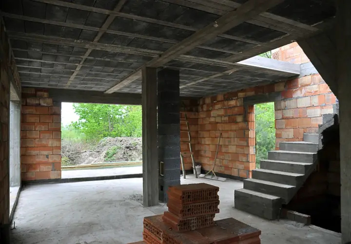 Budowa domu w stanie surowym. Widać betonowy strop, ściany z pustaków ceramicznych, schody i materiały budowlane.