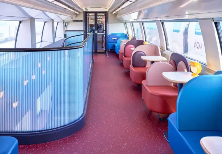 Wnętrze pociągu TGV inOui z kolorowymi siedzeniami i stolikami.