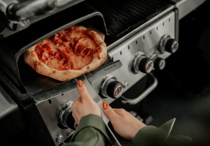 Pizza na grillu, jak piec bez kamienia. Ręka z paznokciem w kształcie pizzy zbliża się do gorącego dania.