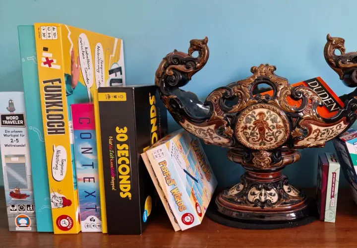 Brettspiele wie "Funkloch" und "30 Seconds" warten darauf, dass ihr Wort erraten wird. Ein Duden-Buch liegt daneben.