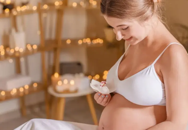 Uśmiechnięta ciężarna kobieta trzyma kwiat. Delikatne światła tworzą atmosferę relaksu, idealną dla kosmetyków dla kobiet w ciąży.