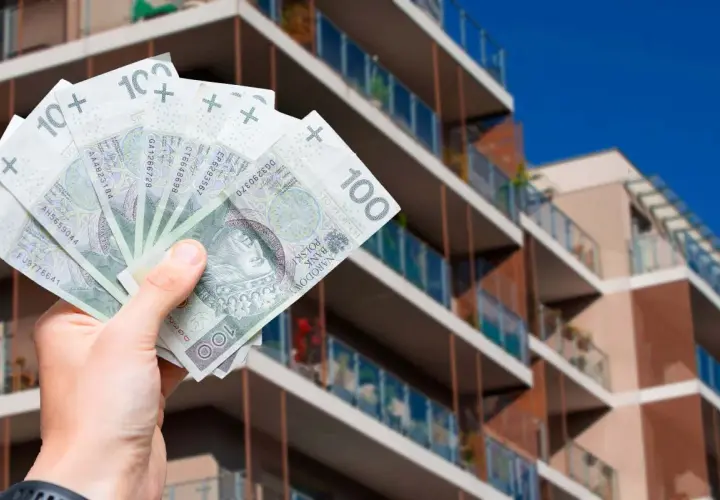 Dłoń trzyma banknoty 100 zł na tle nowoczesnego apartamentowca. Pytanie: jak zapłacić podatek od wynajmu mieszkania?