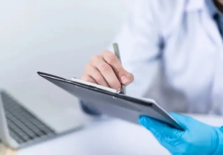 Lekarz w niebieskich rękawiczkach pisze na tablicy, obok laptop.