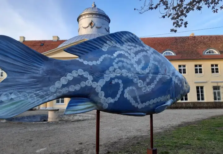 Niebieska rzeźba ryby z perłami zdobi teren w Dolinie Baryczy, idealne miejsce na trasy spacerowe.