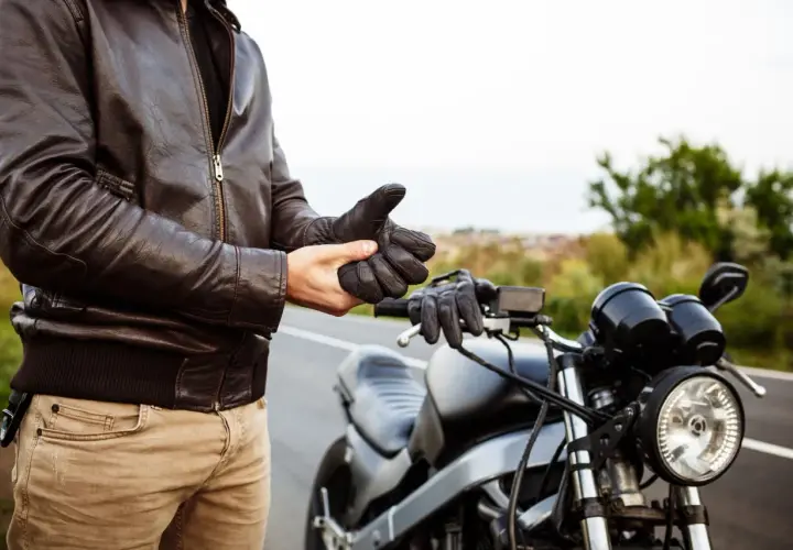 Hombre con chaqueta de cuero se pone guantes junto a una moto. ¿Listo para vender moto sin papeles?