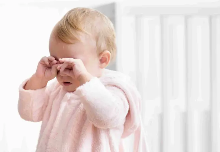 Un neonato con un pigiamino rosa strofina gli occhi, forse un occhio che lacrima per la stanchezza o un piccolo pianto.