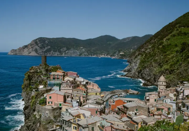 Colorful houses cling to the cliffs of the Cinque Terre Italy coast, overlooking a vibrant blue sea. A medieval tower stands guard.
