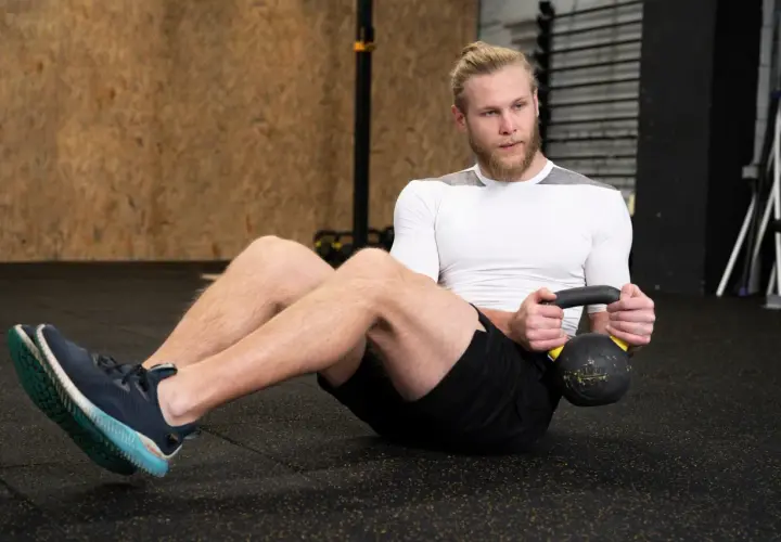Mężczyzna wykonuje brzuszki z obciążeniem, trzymając kettlebell.