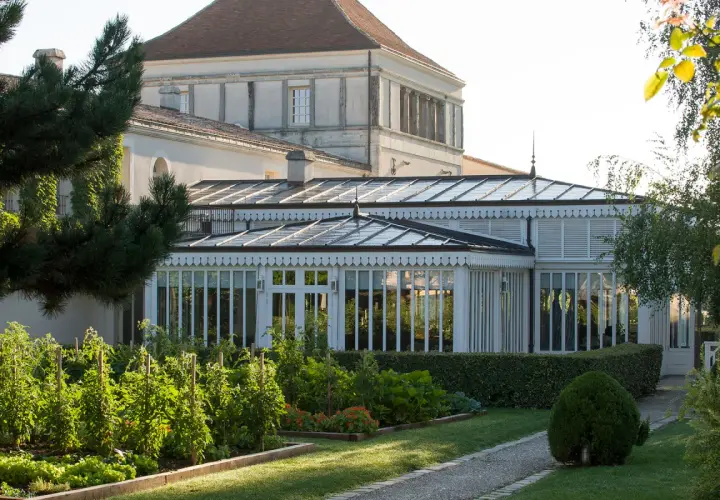 Jardin luxuriant devant une serre élégante, rappelant la beauté du caudalie vignoble.