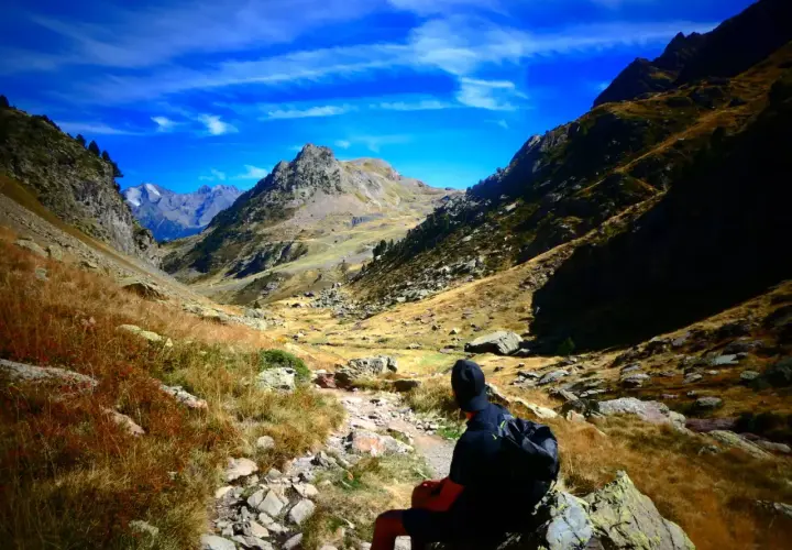 Senderista contempla la inmensidad de los montes Pirineos bajo un cielo azul intenso.
