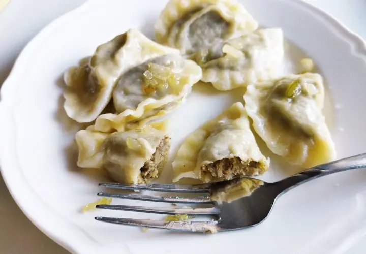 Pyszne pierogi z soczewicą na białym talerzu, jeden nadgryziony, obok widelec.