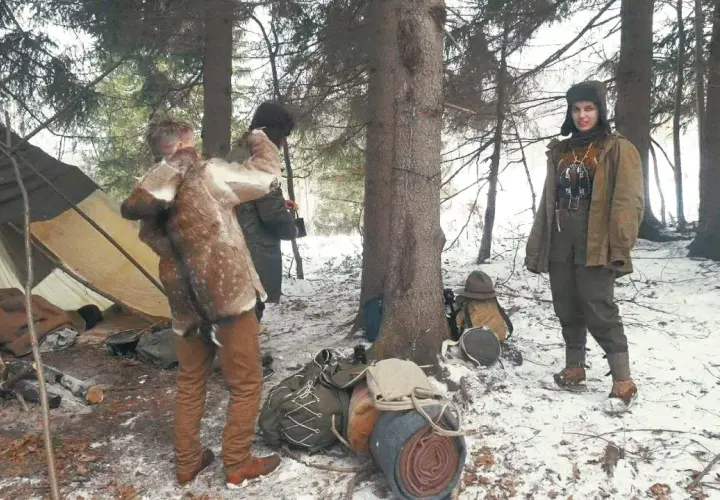 Zimowy obóz w lesie, namiot, ekwipunek i ludzie w strojach nawiązujących do bushcraftu. To właśnie bushcraft co to za przygoda!