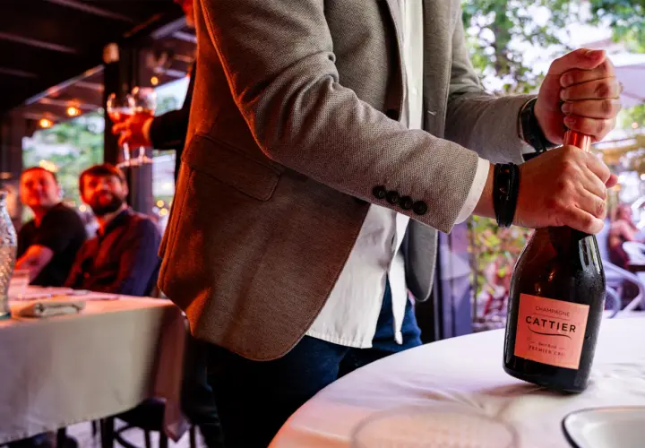 Mężczyzna otwiera butelkę szampana Cattier. Różnica między prosecco, cavą i szampanem tkwi w metodzie produkcji.