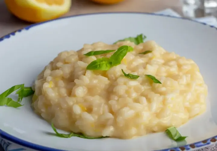 Kremowe risotto cytrynowe, ozdobione listkami bazylii, na talerzu z cytryną w tle.