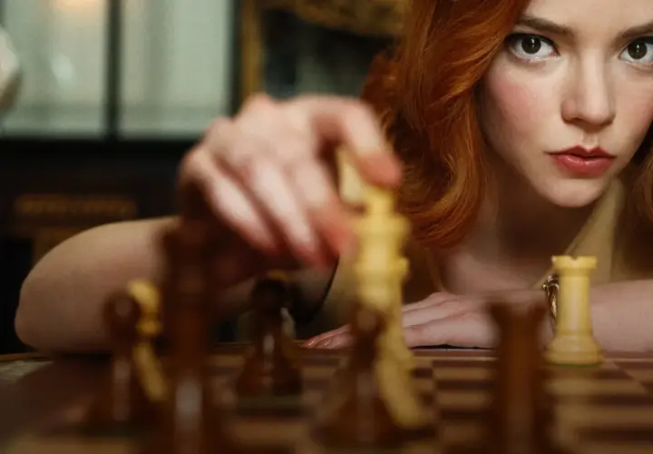 Anya Taylor-Joy jako Beth Harmon w "Gambicie Królowej" wykonuje ruch figurą na szachownicy.