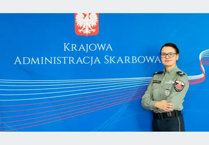 Kobieta w mundurze służby celno-skarbowej stoi przed niebieskim tłem z napisem "Krajowa Administracja Skarbowa".