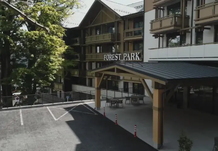 Elegancki hotel 5 gwiazdkowy Forest Park otoczony zielenią, z parkingiem i zadaszonym wejściem.