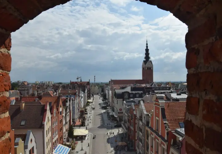 Widok na ulicę i kamienice w **starym mieście Elbląg**. W oddali widać wieżę kościoła.