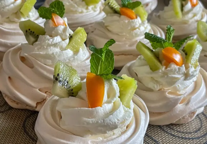 Pyszne gniazdka bezowe z kremem mascarpone, ozdobione kawałkami kiwi, pomarańczy i listkami mięty.