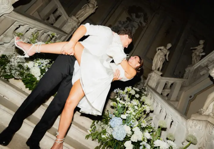 Un couple s'embrasse passionnément lors de leur mariage chez soi, entouré de fleurs blanches et bleues sur un escalier orné de statues.