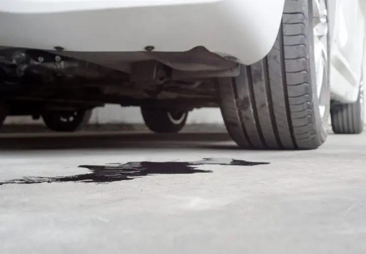 Macchia scura sul cemento sotto un'auto, probabile perdita liquido radiatore.