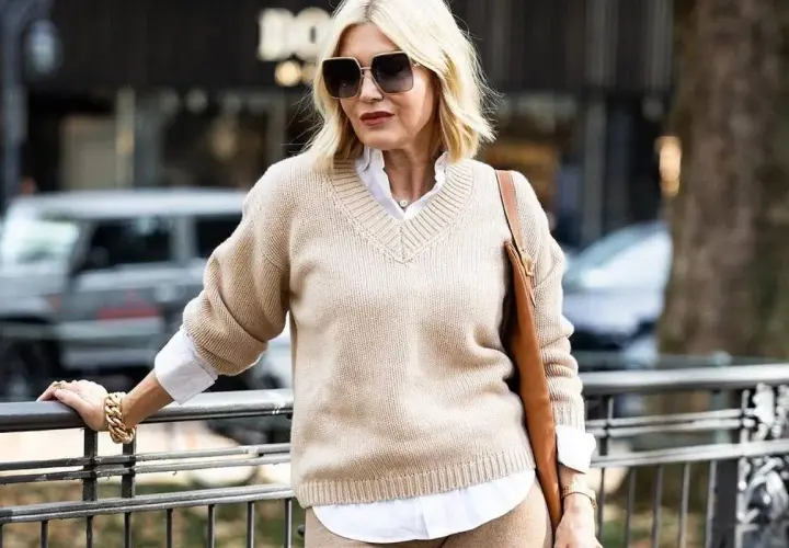 Elegancka kobieta po 50-tce w beżowym swetrze i białej koszuli. Stylowa moda dla 50 latki.
