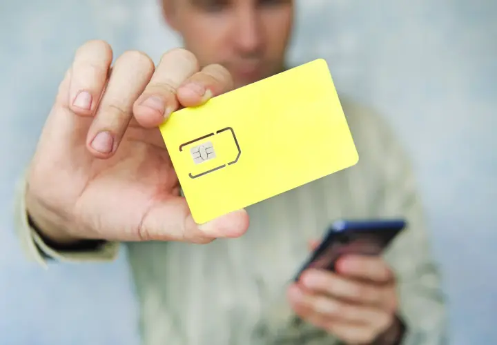Mężczyzna trzyma żółtą kartę SIM i telefon, pokazując, jak zapisać kontakty na karcie sim.