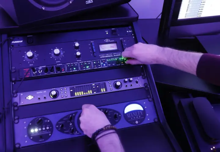 Main d'un ingénieur du son ajustant les potentiomètres d'un rack d'équipement audio, en pleine action de mastering musique.