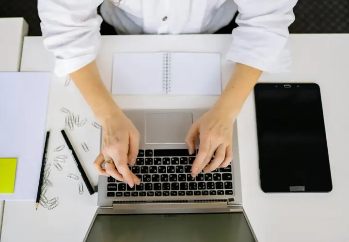 Kobieta pisze na laptopie, szukając informacji, jak napisać stopnie Celsjusza w Excelu. Obok leżą tablet, notatnik i spinacze.