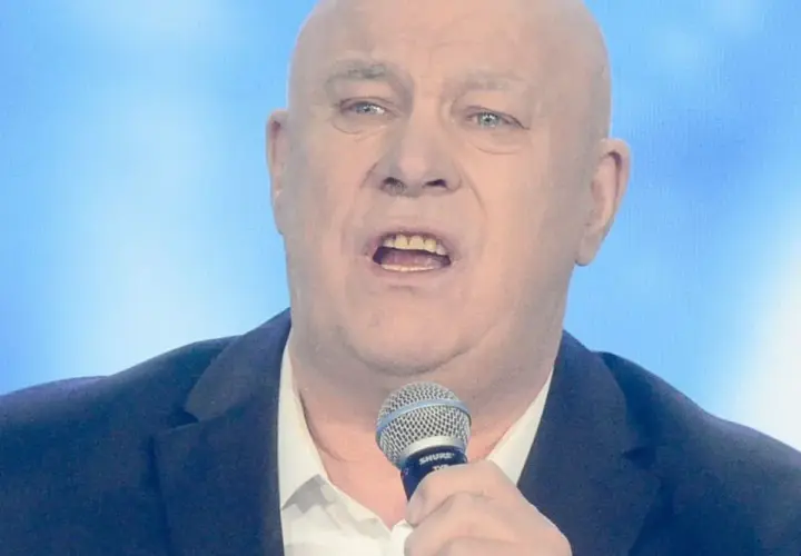 Ryszard Rynkowski śpiewa, trzymając mikrofon. Jego charakterystyczne utwory poruszają serca słuchaczy.