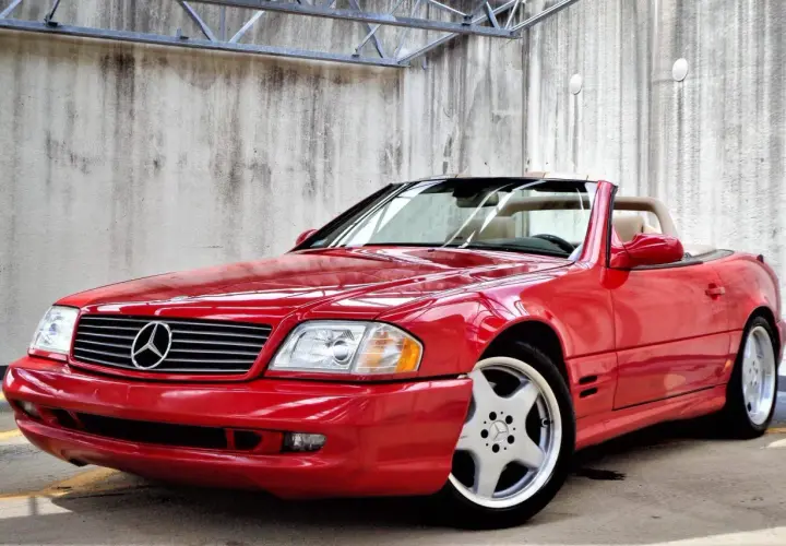 Czerwony kabriolet Mercedes-Benz SL500 z beżowym wnętrzem, zaparkowany przy betonowej ścianie.