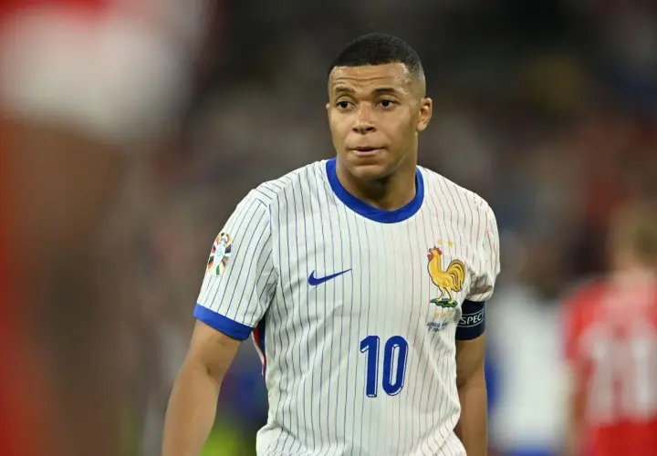 Kylian Mbappé w białej koszulce z numerem 10 i symbolem koguta, reprezentujący Francję. Jego obecne drużyny to PSG i reprezentacja Francji.
