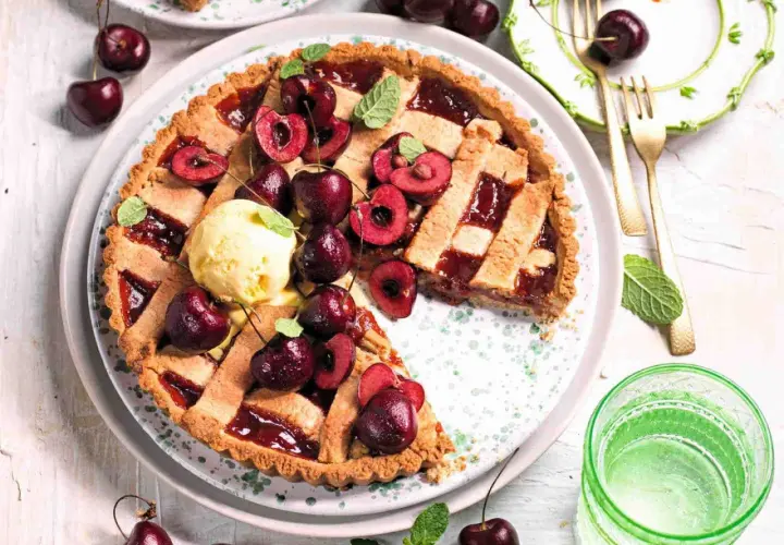 Una deliziosa crostata di ciliegie, guarnita con ciliegie fresche, gelato alla vaniglia e foglioline di menta. Perfetta per un dolce estivo.