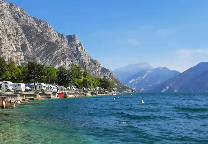 Malowniczy widok na jezioro Garda z campingiem, kamienistym brzegiem i górami w tle. Idealne miejsce na wakacje.