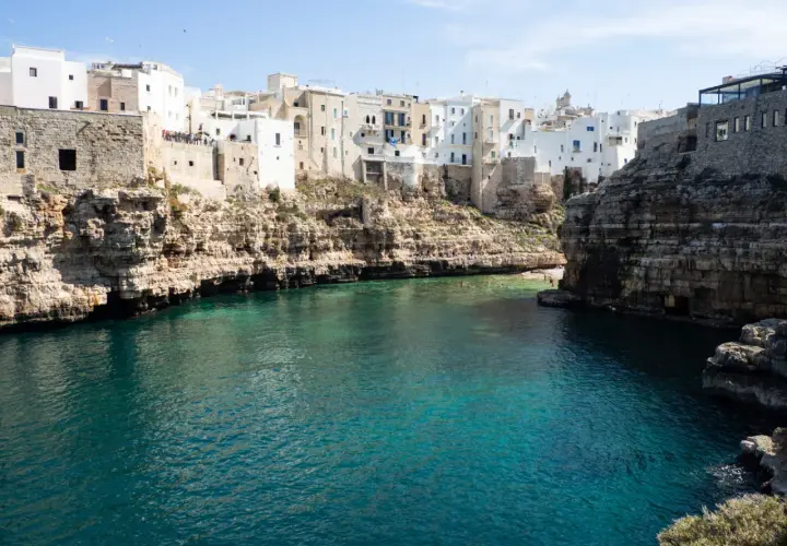 Un estany gento con aguas cristalinas rodea un pueblo blanco construido sobre acantilados rocosos.
