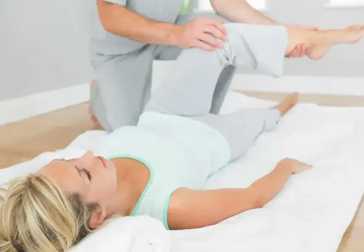 Fizjoterapeuta wykonuje test Patricka na leżącej kobiecie, delikatnie unosząc jej nogę.