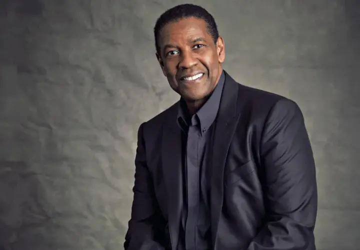 Ritratto di Denzel Washington, attore e doppiatore, con un sorriso caloroso e un abito scuro.