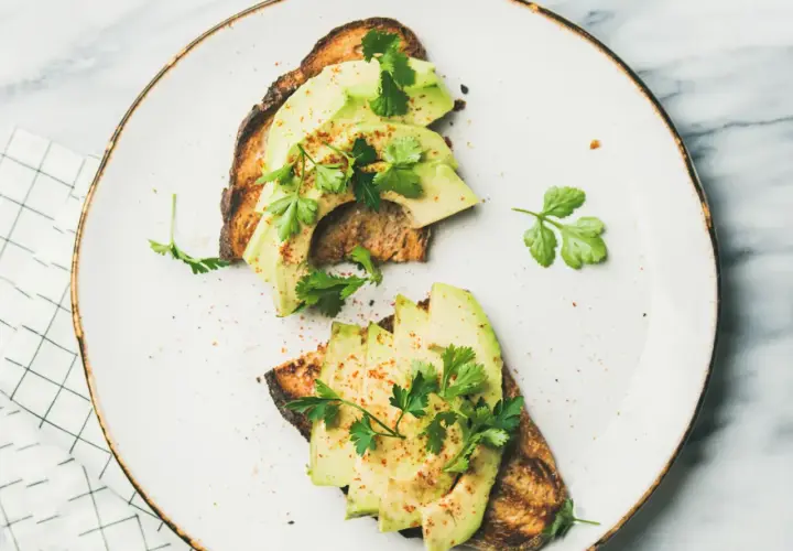 Deux toasts avec avocat tranché, persil frais et une pincée d'épices. Un avocat avec quoi, un délice simple et sain.