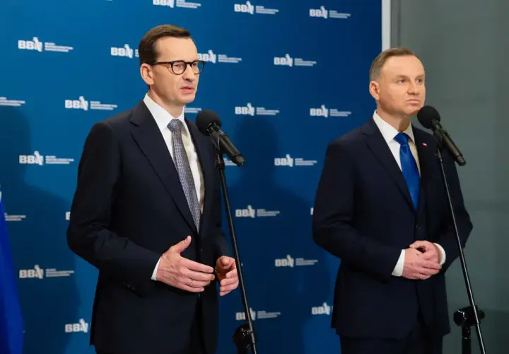 Mateusz Morawiecki i Andrzej Duda stoją przy mikrofonach. Andrzej Duda wzrostem przewyższa premiera.