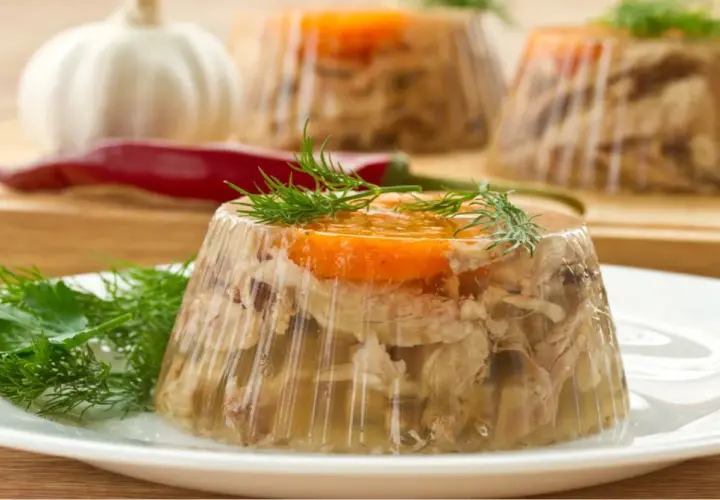 Gotowany schab w galarecie, ozdobiony marchewką i koperkiem, prezentuje się apetycznie na talerzu.