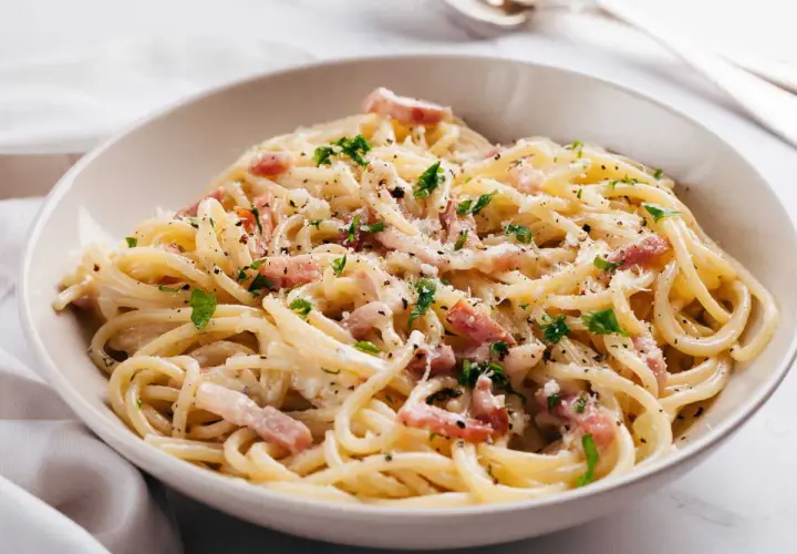 Un plat de pâtes à la carbonara crémeuses, garni de lardons, de parmesan râpé et de persil frais. Un délice italien.