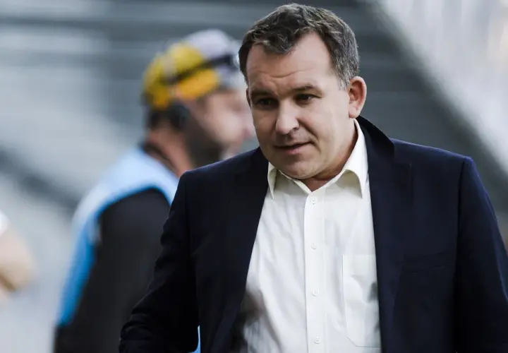 Żyżyński dziennikarz sportowy w garniturze, z uwagą obserwuje wydarzenia na boisku.
