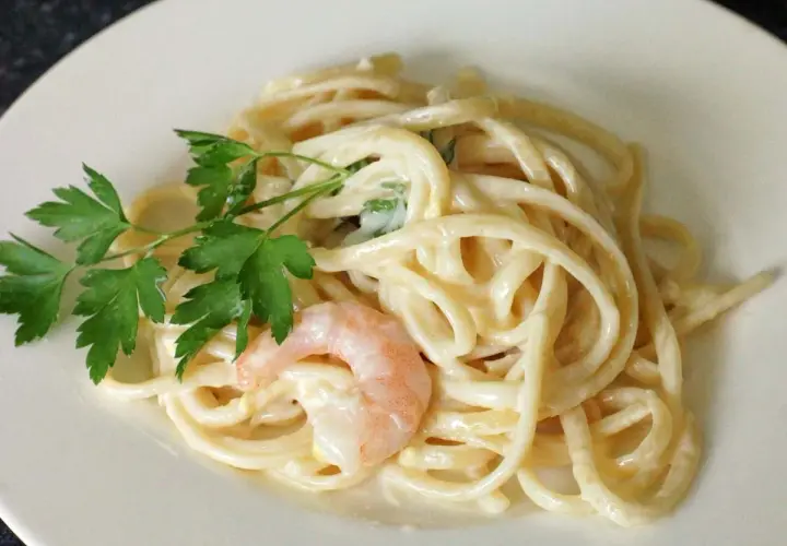 Cremige Pasta al Limone mit Garnelen und Petersilie auf einem weißen Teller. Ein Genuss für Augen und Gaumen.