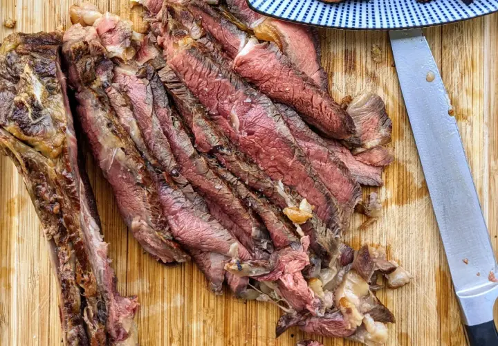 Tranches de bœuf juteuses, parfaitement cuites par la méthode du reverse searing, sur une planche en bois. Un couteau est à côté.