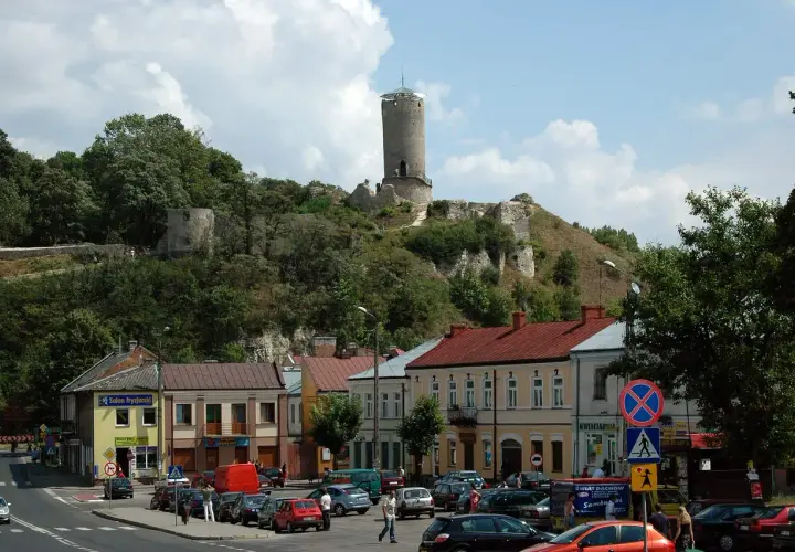 Ruiny iłża zamek górują nad miasteczkiem. W dole widać ulicę z samochodami i kolorowe kamienice.