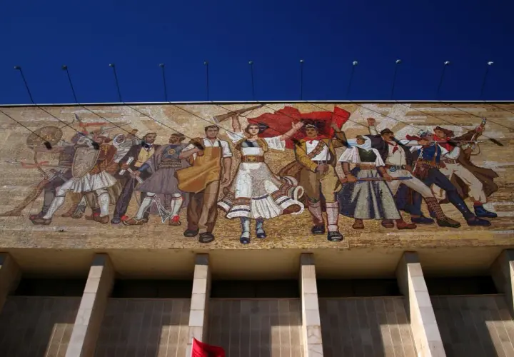 Socrealizm co to? Wielki mozaikowy mural przedstawiający ludzi w strojach ludowych i wojskowych, z flagami i bronią, symbolizujący walkę i jedność.