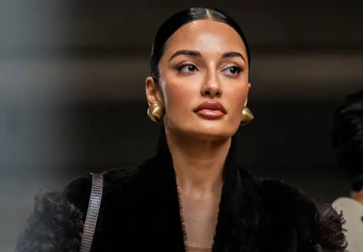 Mujer con peinado pulido y maquillaje natural, luciendo aretes dorados y un abrigo negro de pelo. Su **clean look** irradia elegancia.