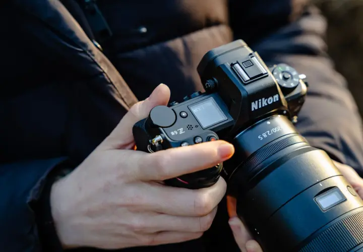 Dłonie trzymają aparat Nikon Z6 III z obiektywem.