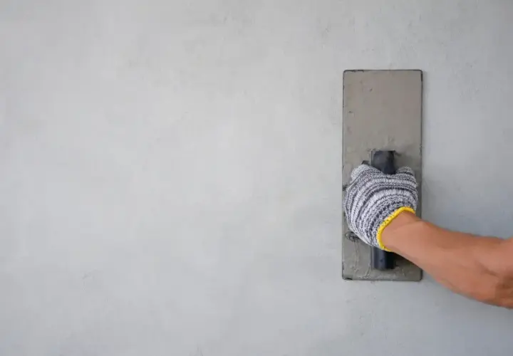 Mano con guanto che esegue la rasatura di un muro con una cazzuola.